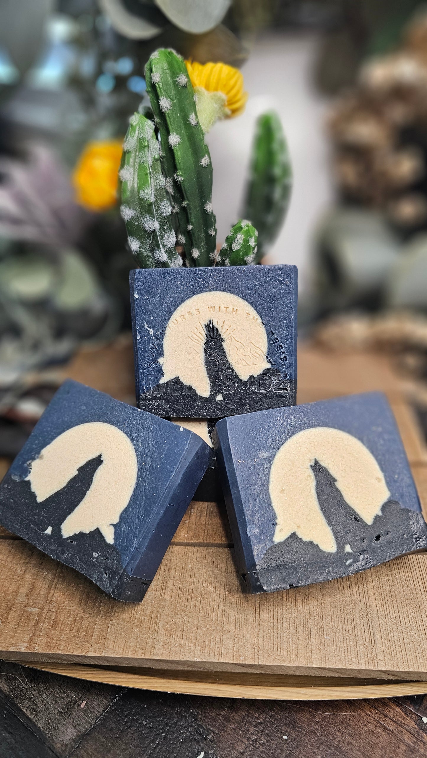 Rectangular handmade soap bars, featuring a deep blue and cream color block design with a black wolf silhouette and moon graphic, arranged together on a wooden surface with a blurred cactus in the background