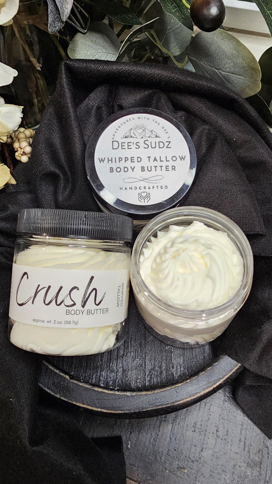 Three clear plastic jars of Dee’s Sudz whipped tallow body butter with black lids, featuring a white whipped texture and labeled CRUSH displayed on a wooden surface.