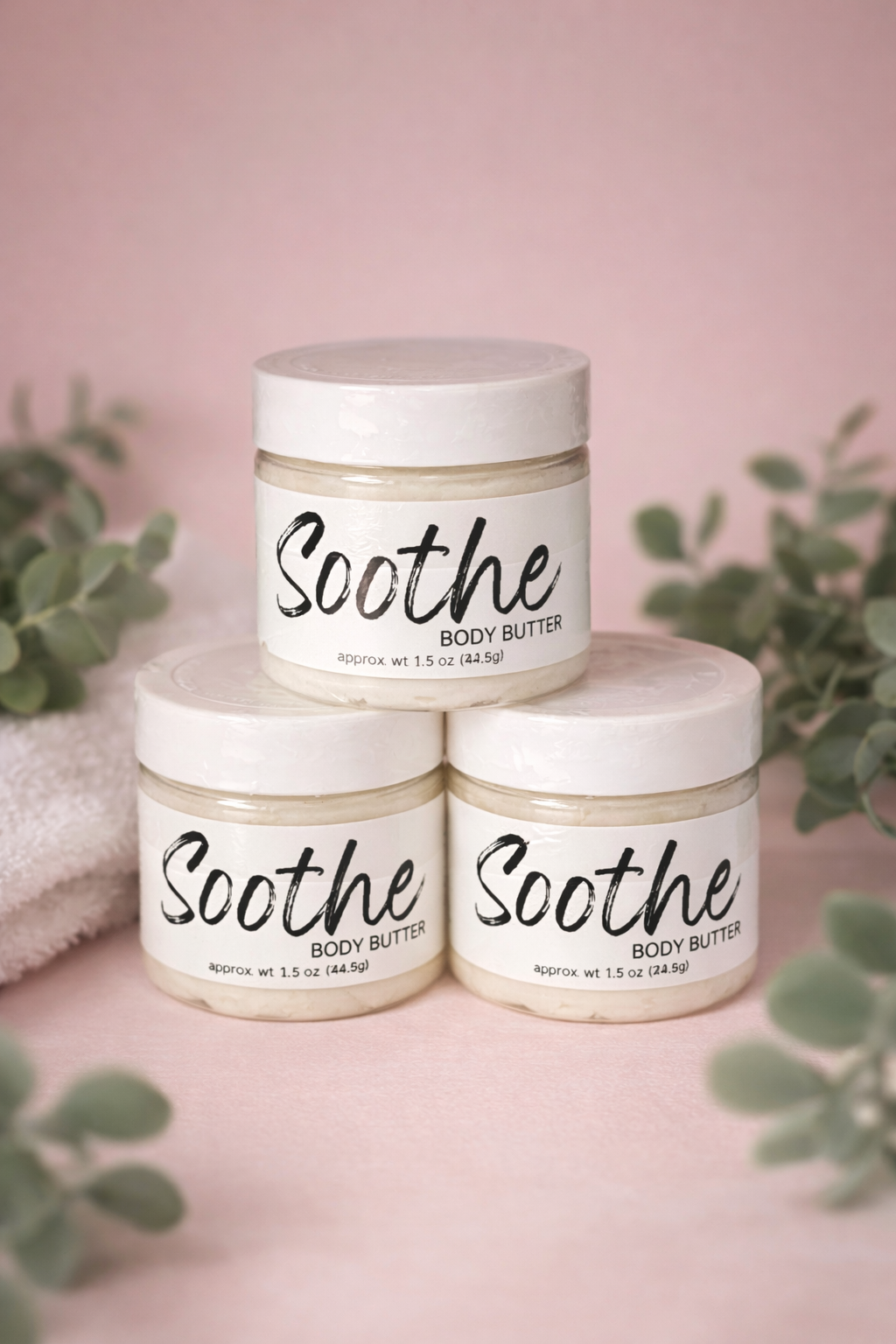 Three stacked jars of Soothe body butter with Dee’s Sudz branding, featuring white lids, cream-colored whipped texture visible through clear jars, and minimalist black script labels against a soft pink background.