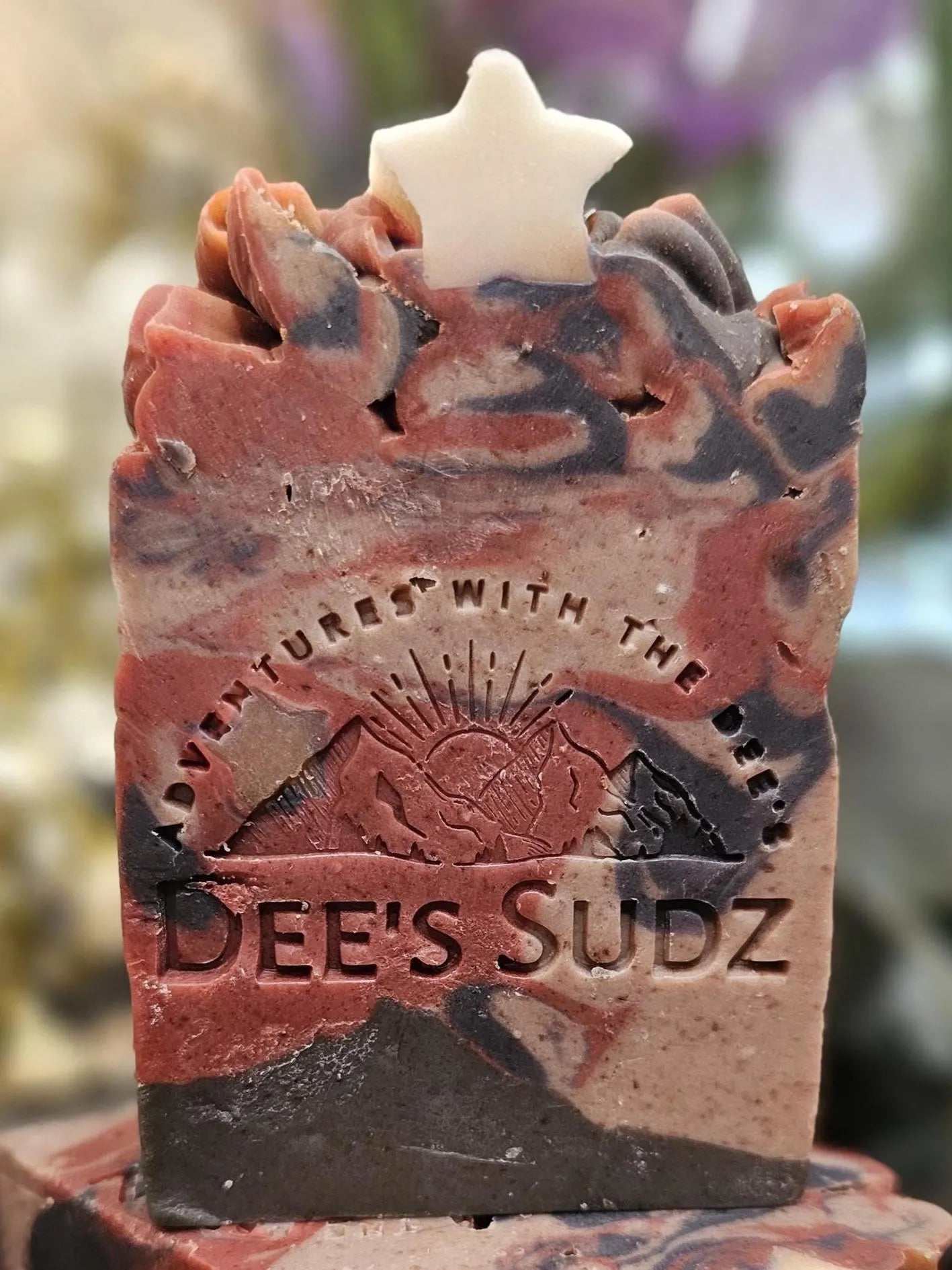 Rectangular handmade soap bar with the Dee’s Sudz logo, featuring a red, charcoal, and cream swirl design with a white star accent on the textured top.