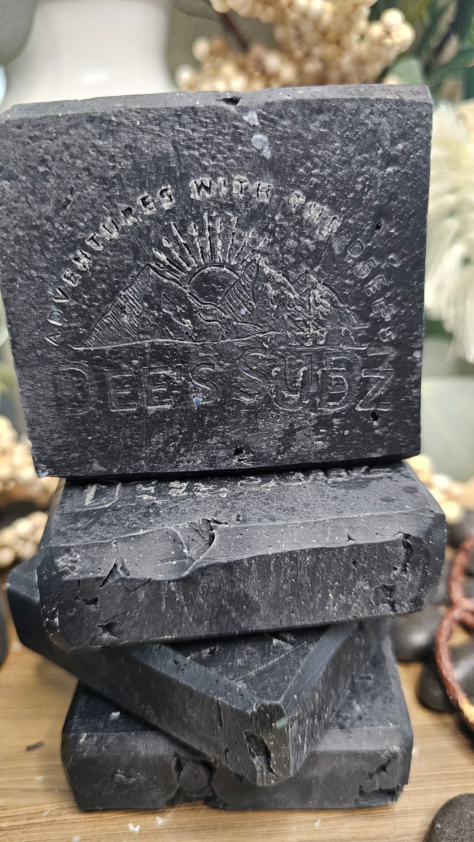 Rectangular handmade soap bars with the Dee’s Sudz logo, featuring a solid charcoal black color, stacked vertically on a wooden surface.