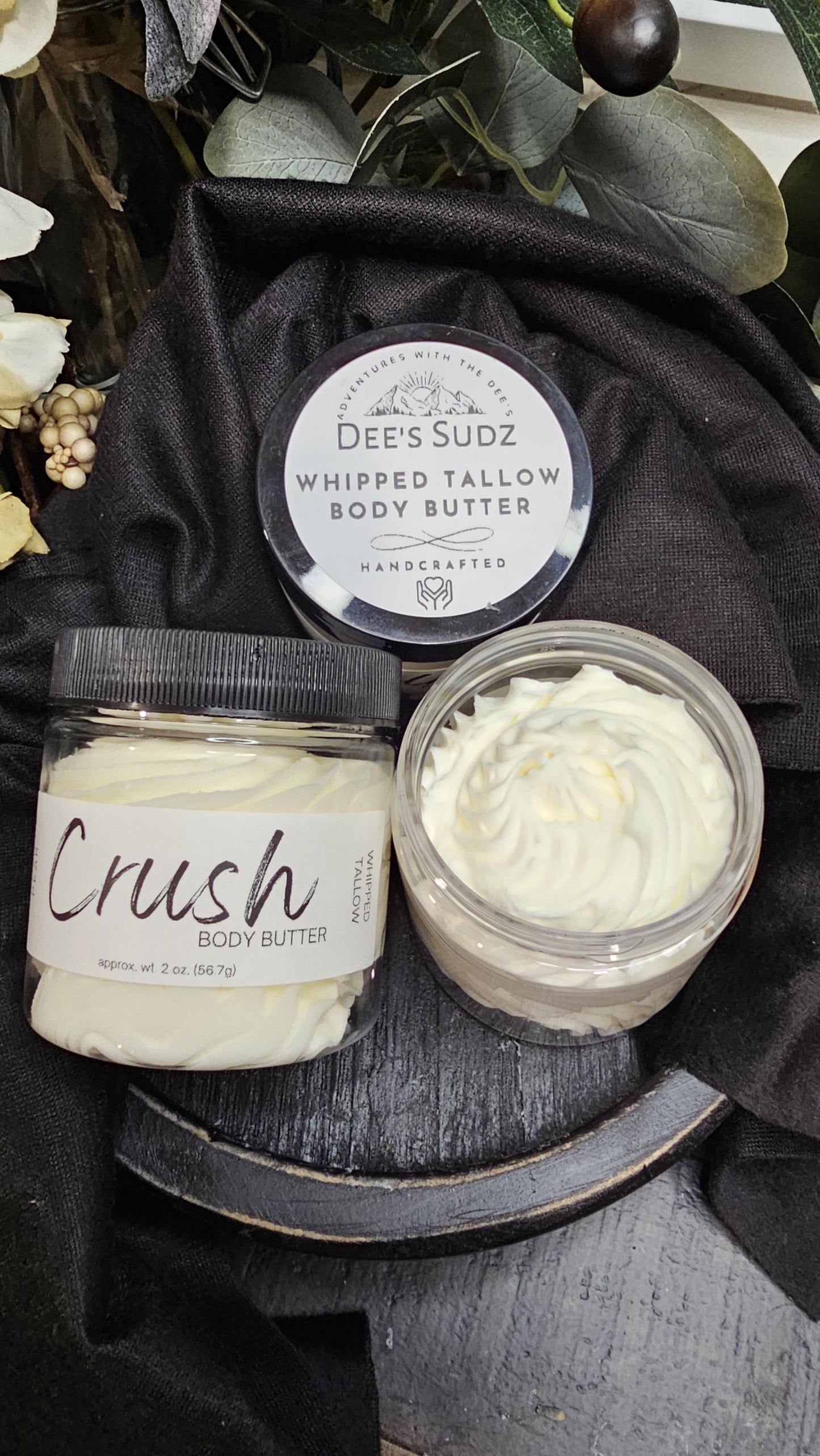 Three clear plastic jars of Dee’s Sudz whipped tallow body butter with black lids, featuring a white whipped texture and labeled CRUSH displayed on a wooden surface.