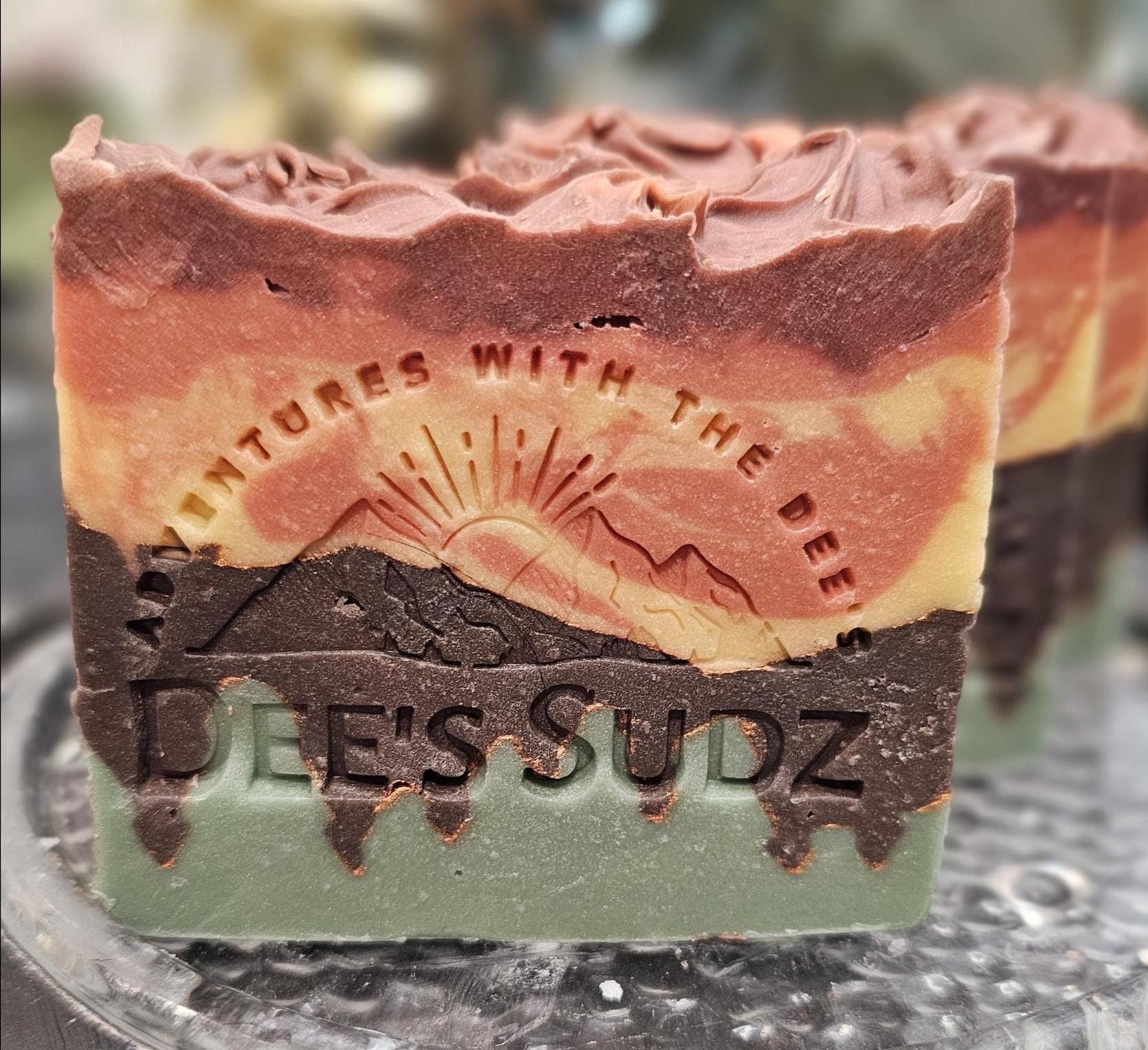 Rectangular handmade soap bar with the Dee’s Sudz logo, featuring layered green, brown, and golden tones with a soft swirl design.