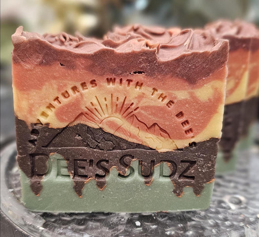 Rectangular handmade soap bar with the Dee’s Sudz logo, featuring layered green, brown, and golden tones with a soft swirl design.