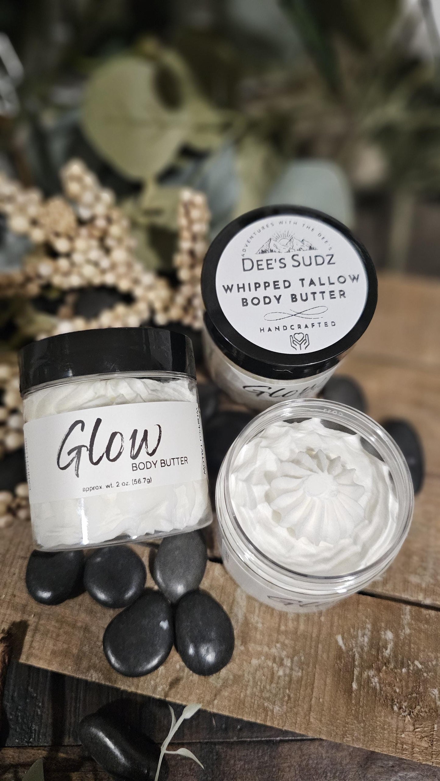 Three clear plastic jars of Dee’s Sudz whipped tallow body butter with black lids, featuring a white whipped texture and labeled GLOW displayed on a wooden surface.