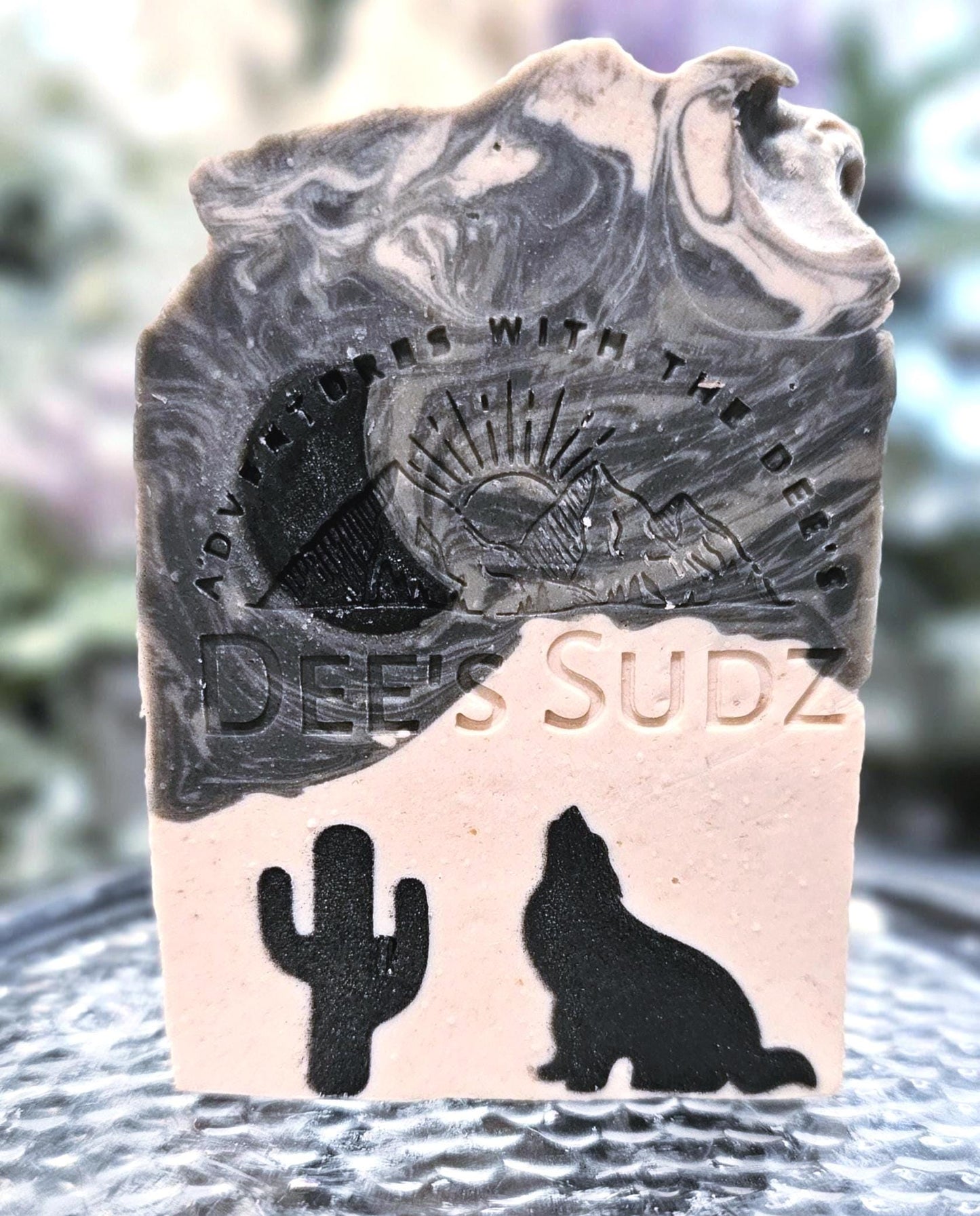 Rectangular handmade soap bar with the Dee’s Sudz logo, featuring a charcoal and cream swirl design with black cactus and wolf & half moon silhouettes on the front.