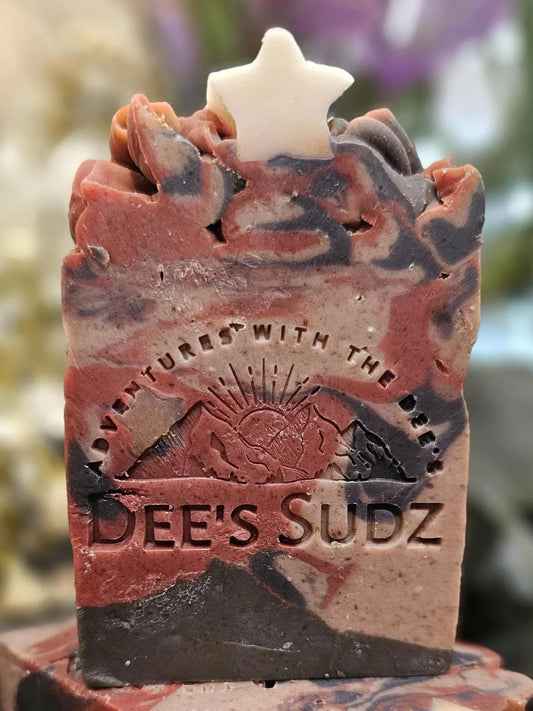 Rectangular handmade soap bar with the Dee’s Sudz logo, featuring a red, charcoal, and cream swirl design with a white star accent on the textured top.
