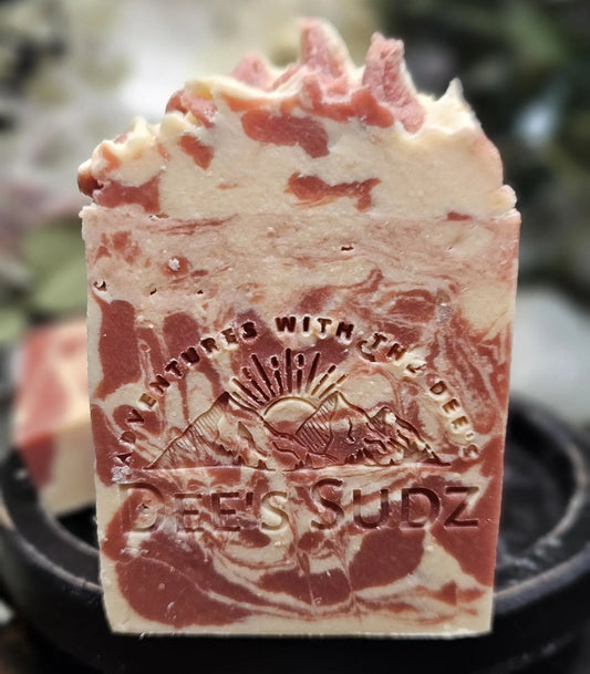 Rectangular handmade soap bar with the Dee’s Sudz logo, featuring a red and cream swirl design with a textured top displayed on a black wood base