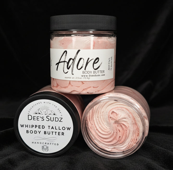 Three clear plastic jars of Dee’s Sudz whipped tallow body butter with black lids, featuring a white whipped texture and labeled Adore displayed on a black velvet surface