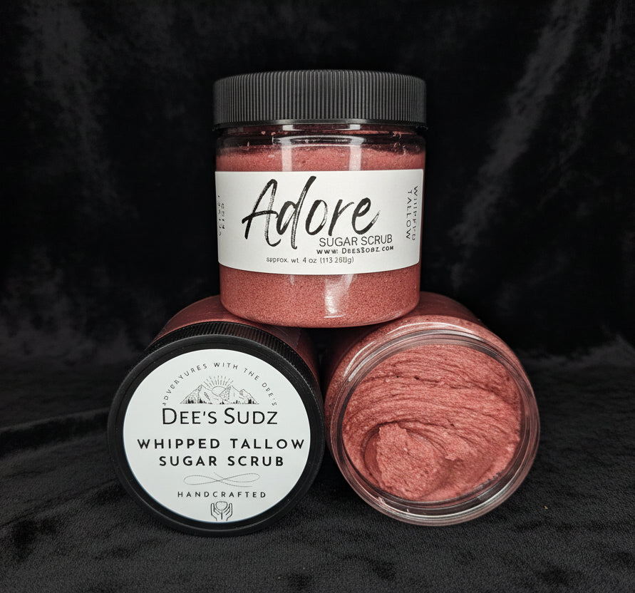 Three clear plastic jars of Dee’s Sudz whipped tallow sugar scrub with black lids, featuring a red whipped texture and labeled containers displayed on a black cloth.
